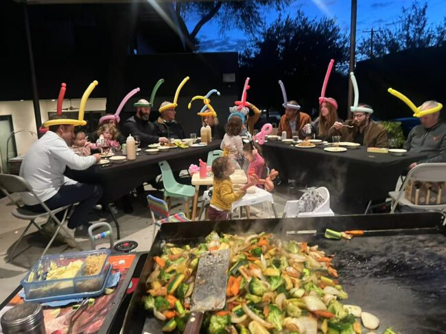 Backyard hibachi birthday dinner setup with balloon decorations and guests seated around the grill